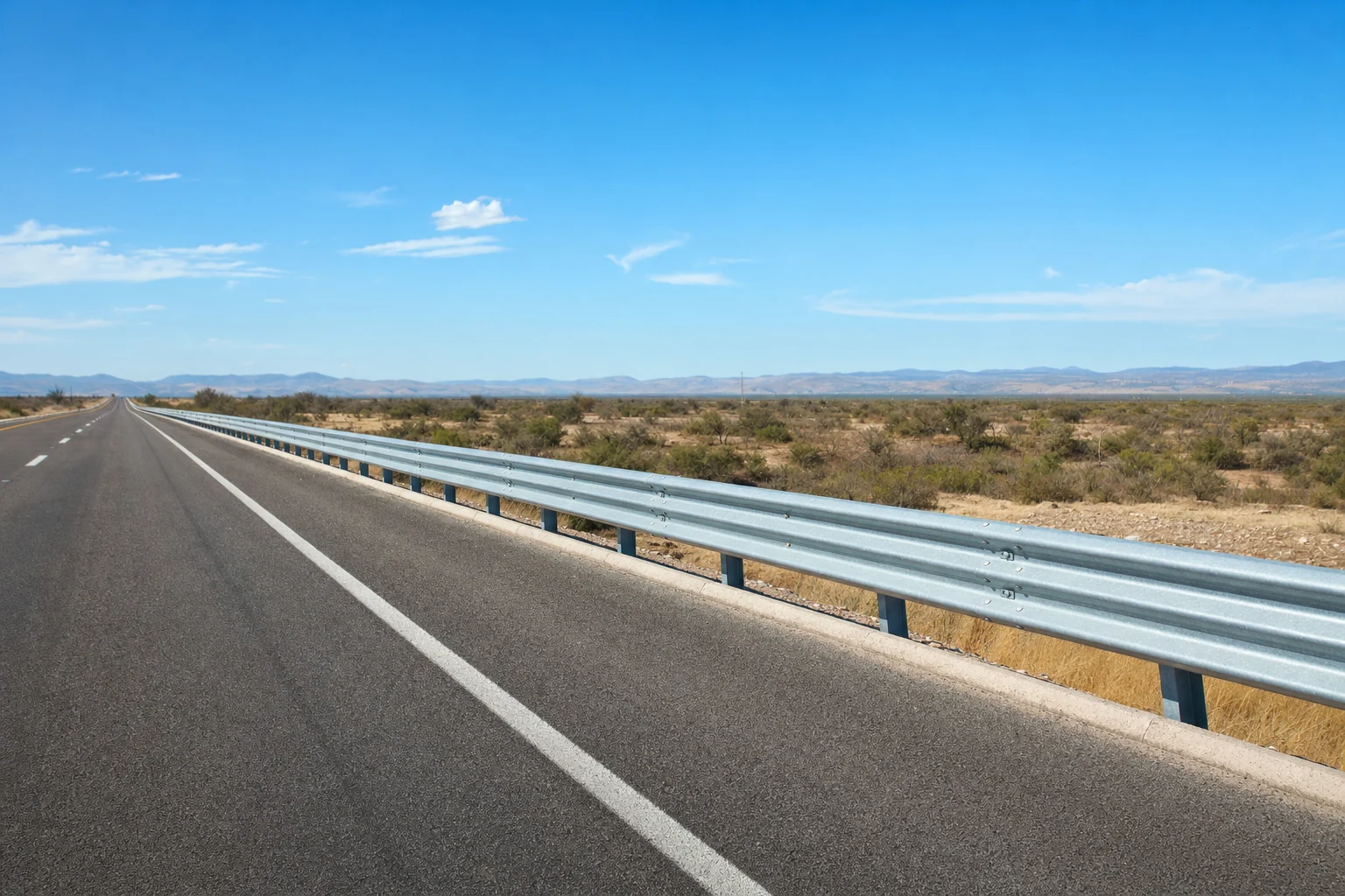 Barrera metálica de contención instalada al costado de una carretera de dos carriles.